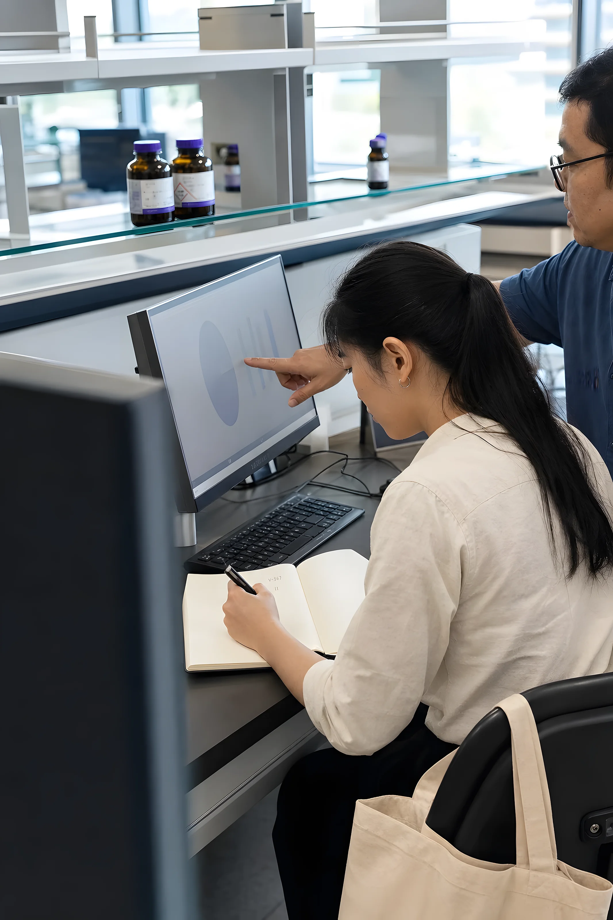 A VKA graduate taking notes as a senior colleague reviews work on screen