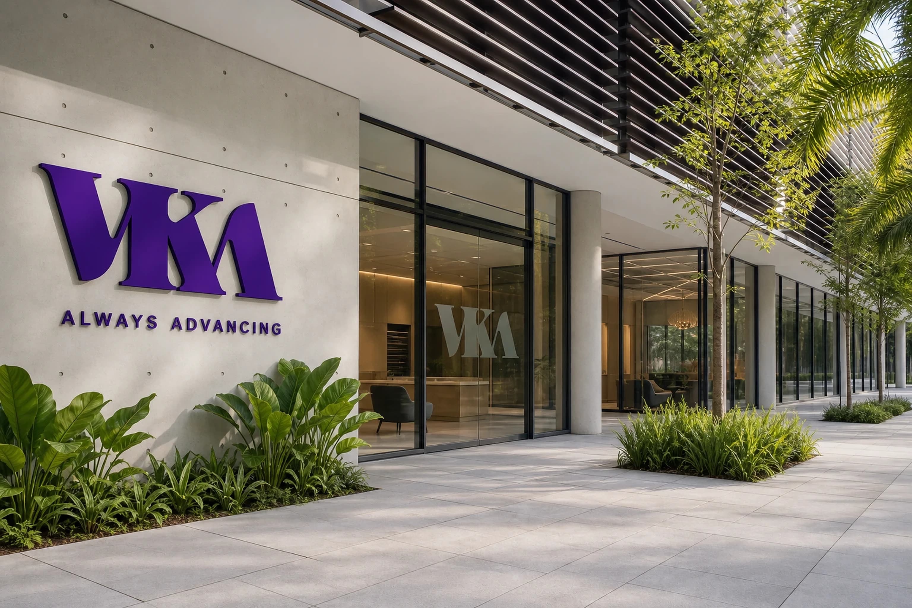 The front of a modern building with a large purple VKA sign above the words Always Advancing, glass walls and planted beds along a paved walkway